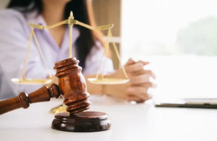 Close-up of a judge's gavel and balance scales with a professional woman in the background, representing legal staffing and justice