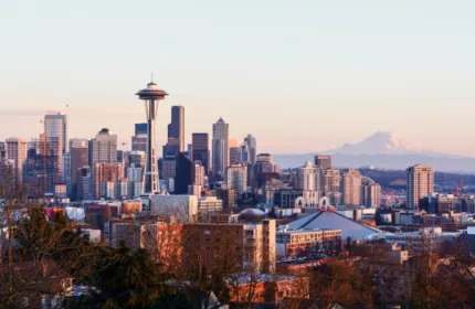 Panoramic view of downtown Seattle at sunrise with the Space Needle in the foreground and Mount Rainier in the background, highlighting the city's blend of urban architecture and natural beauty.