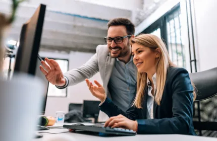 Two professionals collaborating at a computer workstation in a modern office environment.