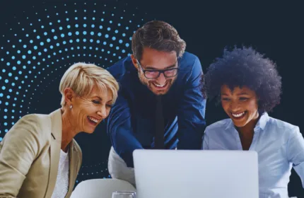 A group of professionals gathered around a laptop reviewing business data in a modern office setting.