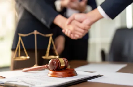 Legal professionals shaking hands over a signed document with a gavel and scales of justice on a desk