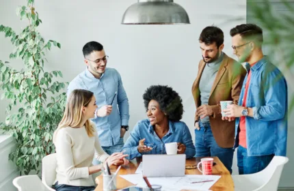Five professionals gathered around a table with a laptop and documents, actively discussing insights, representing market intelligence, collaboration, and informed decision making for LPCs and LMHCs.