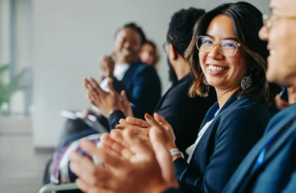 Professionals seated together applauding during a workplace recognition event.