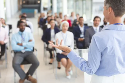 Presenter speaking to a group of professionals during a corporate seminar in a modern conference room.