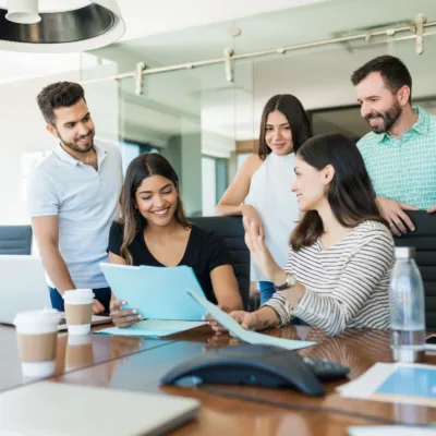 Five professionals gathered around a table reviewing documents and a laptop in an office, representing strategic resourcing and collaboration to maintain operational continuity during companywide restructuring.