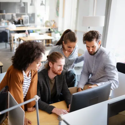 Four professionals gathered around a computer in an office reviewing documents together, representing strategic intervention to optimize accounts payable operations and improve team efficiency.
