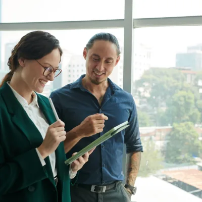Two professionals standing by a window reviewing a tablet together, representing persistent outreach and collaboration driving success in a dedicated resource program.