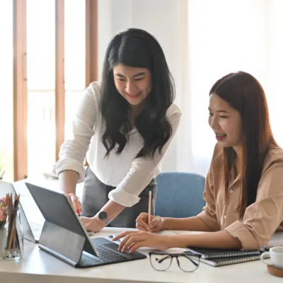 Two professionals working together at a desk reviewing information on a laptop and taking notes, representing support for a smooth financial leadership transition through a dedicated resource solution.
