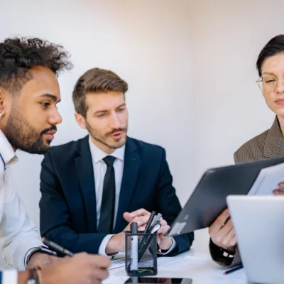 Three professionals seated at a table reviewing documents and a tablet together, representing financial leadership support and securing a controller role through a dedicated resource program.