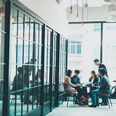 Team of professionals seated around a table working on laptops and documents in a glass-walled office, representing expert support for managed review and document production processes.