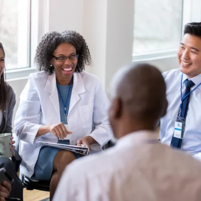 Group of professionals in a meeting with a healthcare professional in a lab coat reviewing notes, representing building a medical affairs team and supporting growth after acquisitions.