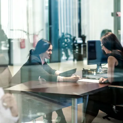 Two professionals seated across a desk reviewing documents and writing notes, representing fast sourcing, onboarding, and project kickoff for a project management role.