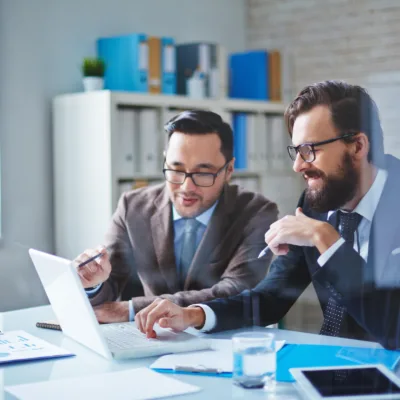 Two professionals seated at a desk collaborating over a laptop and documents, representing trusted administrative support and high-caliber executive assistant talent delivering long-term business impact.