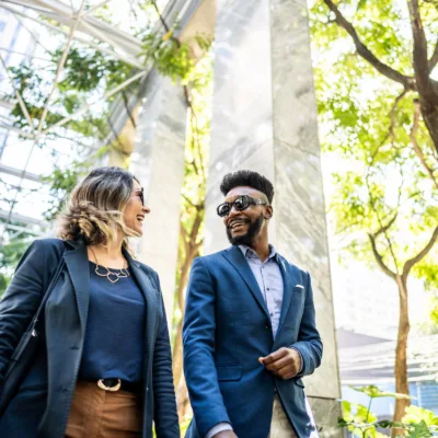 Two professionals walk together outdoors while conversing, representing networking, collaboration, and workplace connection.