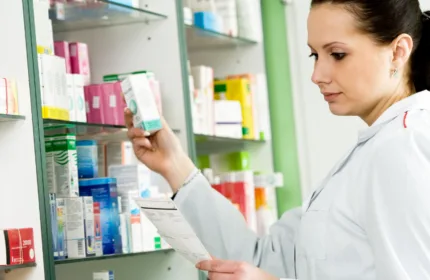 Female pharmacists in white coat reading prescription and pulling medication box off of shelf