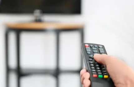 A person holding a TV remote pointed at a TV.