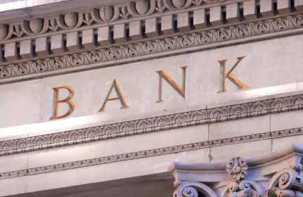 Close-up of a classical bank building, showing stone columns and the word “BANK” engraved in large letters above the entrance.