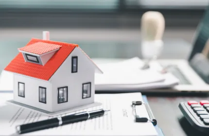 Model house, pen, and contract paperwork on a desk representing property and casualty insurance supported by BH Financial.