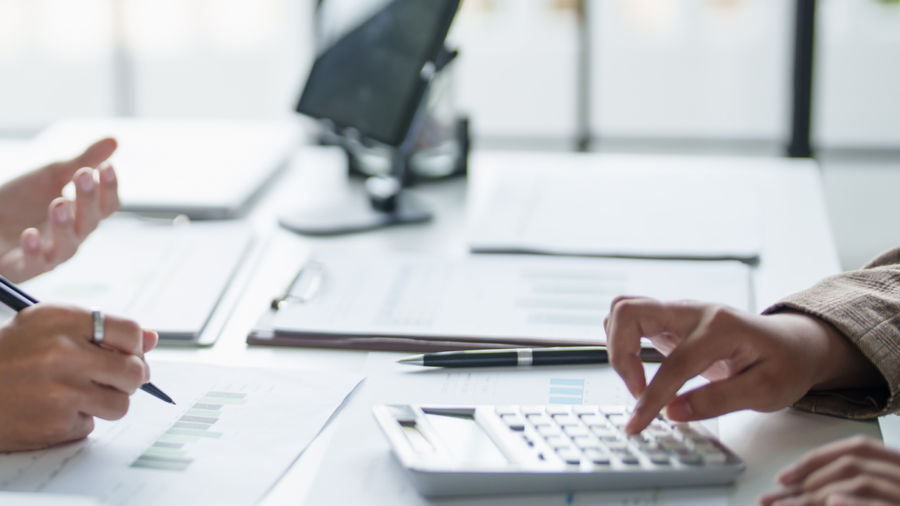 Business professionals reviewing financial charts and documents during an audit, risk, and compliance meeting, with a calculator and tablet on the desk.