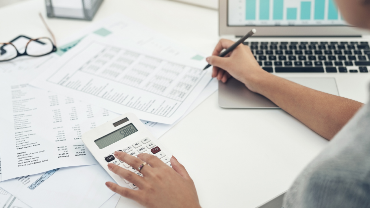 Person reviewing payroll spreadsheets and financial data using a calculator and laptop with charts on the screen.