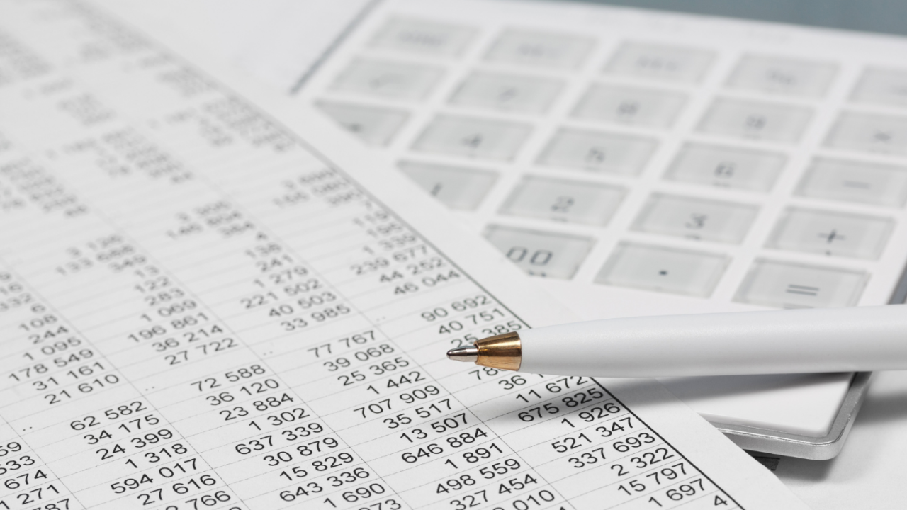Close-up of a financial spreadsheet with numeric data, a white pen, and a calculator, representing taxation and tax-related calculations.