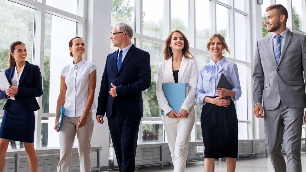 A group of professionals walking together through a bright, modern office hallway, representing coordinated human resources operations and team collaboration.