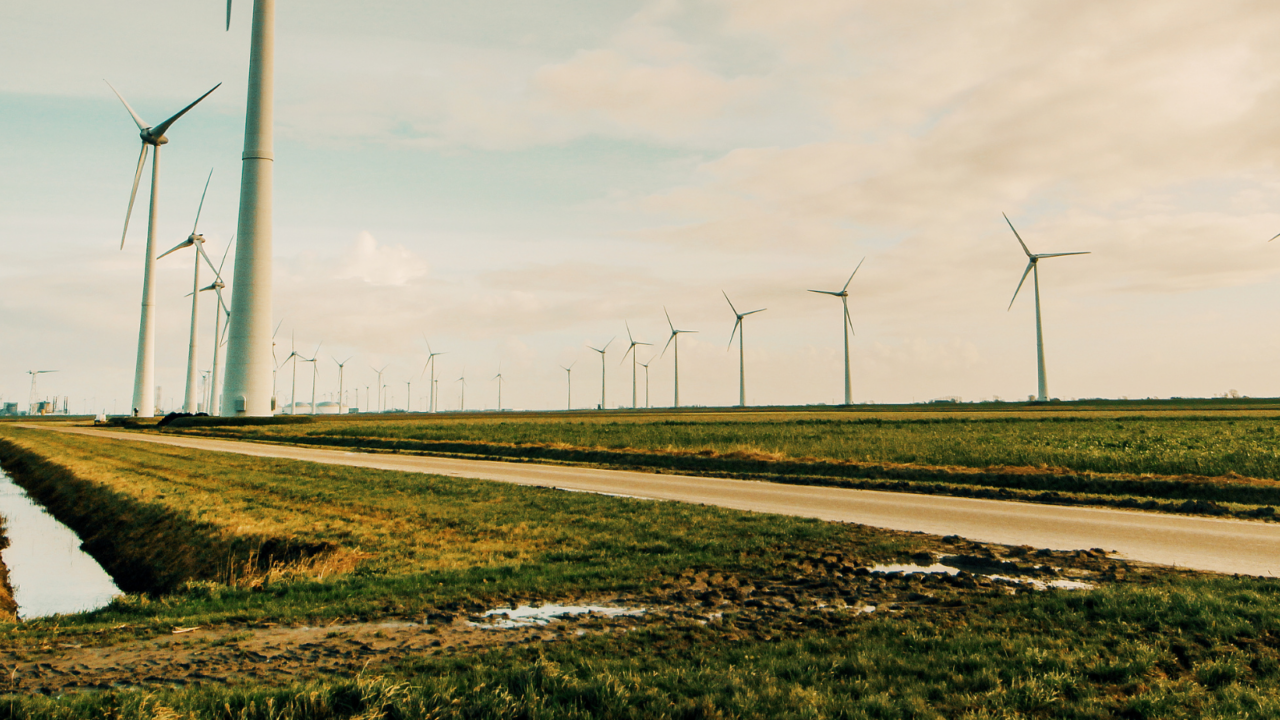 A wide landscape featuring multiple wind turbines spread across green fields under a partly cloudy sky.