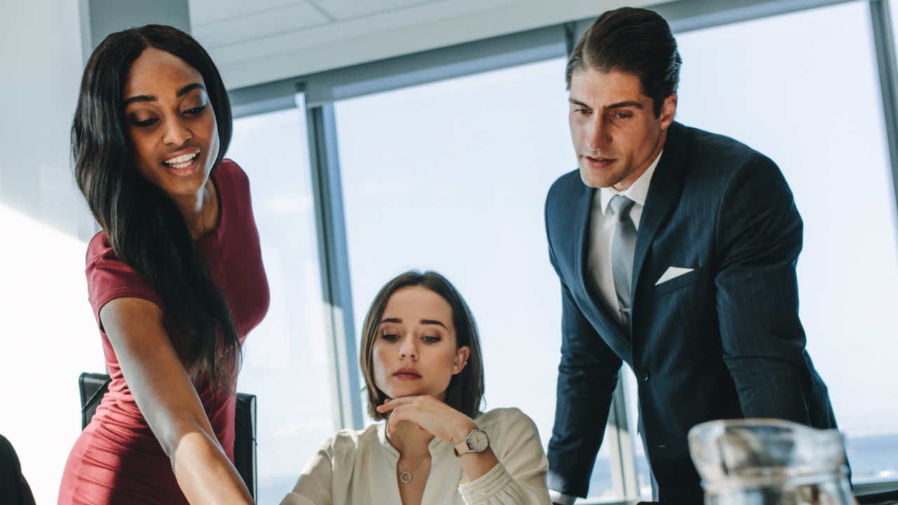 A modern conference room with a round wooden table where several professionals are seated, engaged in discussion.