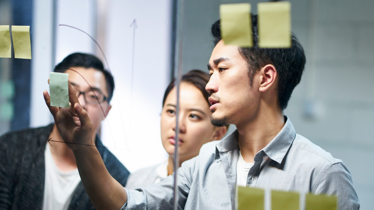 Team members collaborate during an organizational development and change management planning session using sticky notes on a glass board to map ideas and strategic initiatives.