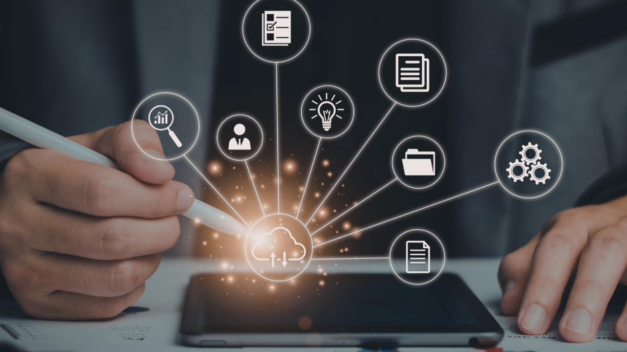 Person using a stylus on a tablet with glowing cloud icon at the center, surrounded by digital strategy elements such as analytics, user profiles, documents, lightbulb for ideas, folder, and gears representing process automation.