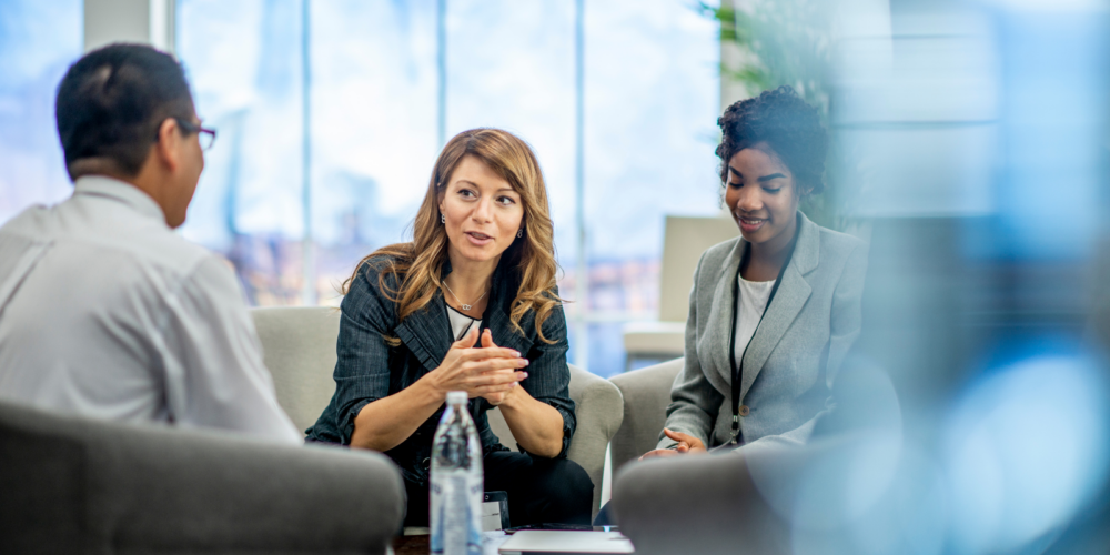 Three professionals seated in a modern office collaborate over financial information, discussing documents and processes related to accounts payable and receivable management.