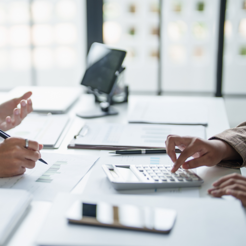Business professionals reviewing financial charts and documents during an audit, risk, and compliance meeting, with a calculator and tablet on the desk.