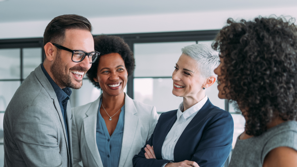Group of business professionals in formal attire engaged in a handshake and discussion inside a modern office setting, symbolizing executive leadership, collaboration, and strategic decision-making.