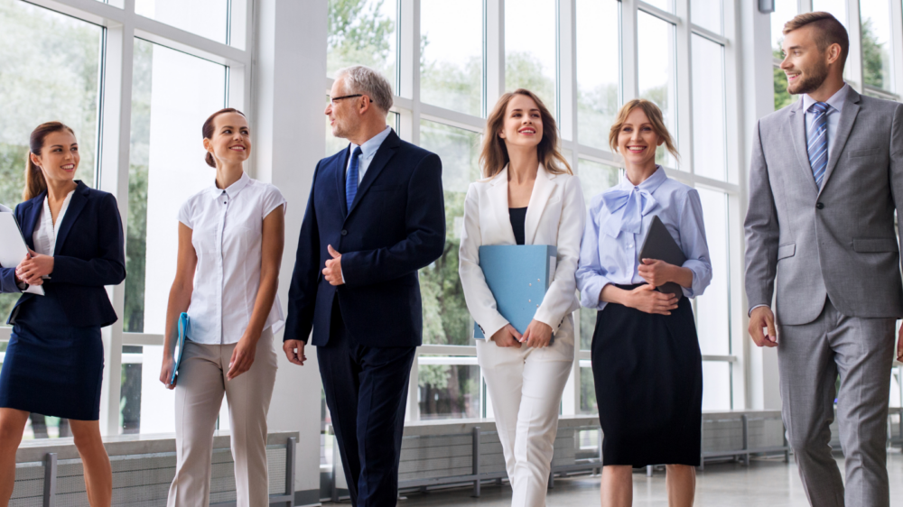 A group of professionals walking together through a bright, modern office hallway, representing coordinated human resources operations and team collaboration.