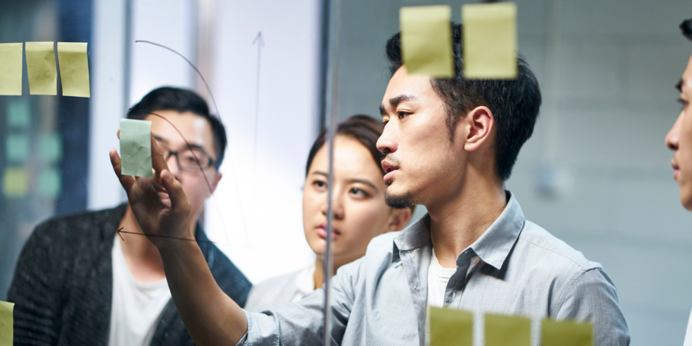 Team members collaborate during an organizational development and change management planning session using sticky notes on a glass board to map ideas and strategic initiatives.