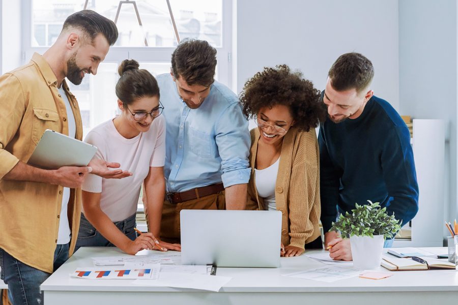 Group of professionals collaborating around a laptop and reviewing charts in a bright office