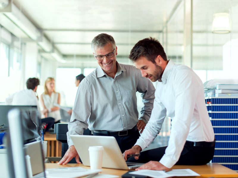Two professionals smiling and reviewing content on a laptop in a bright, modern office setting
