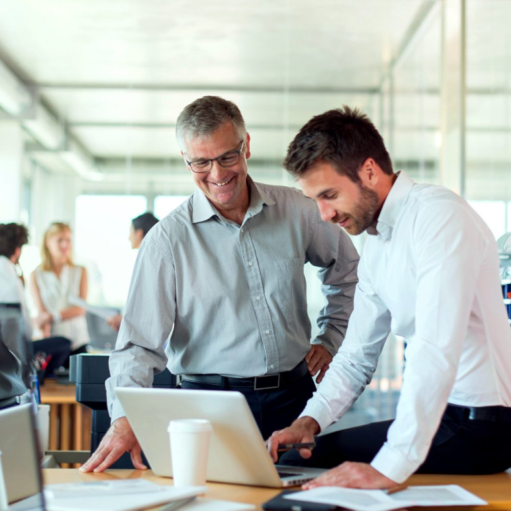Two professionals smiling and reviewing content on a laptop in a bright, modern office setting