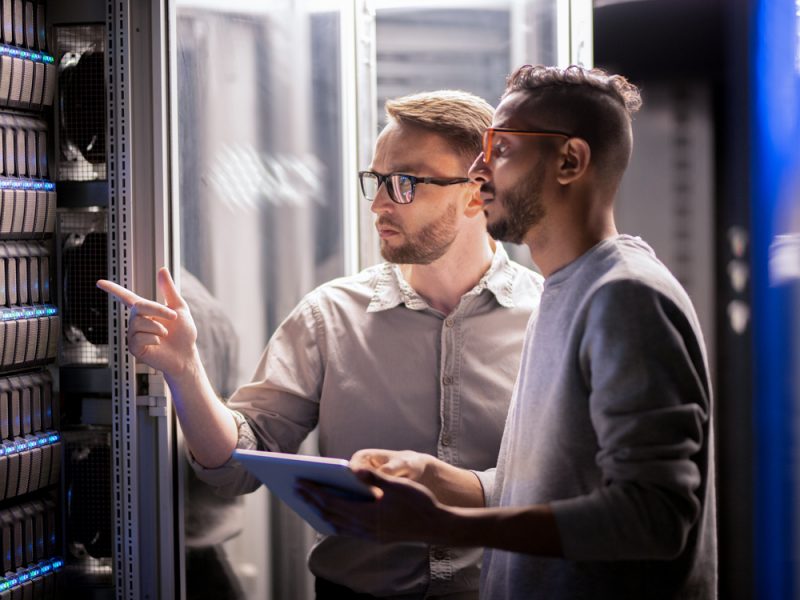 Two male professionals inspecting and discussing server equipment in a secure data center environment