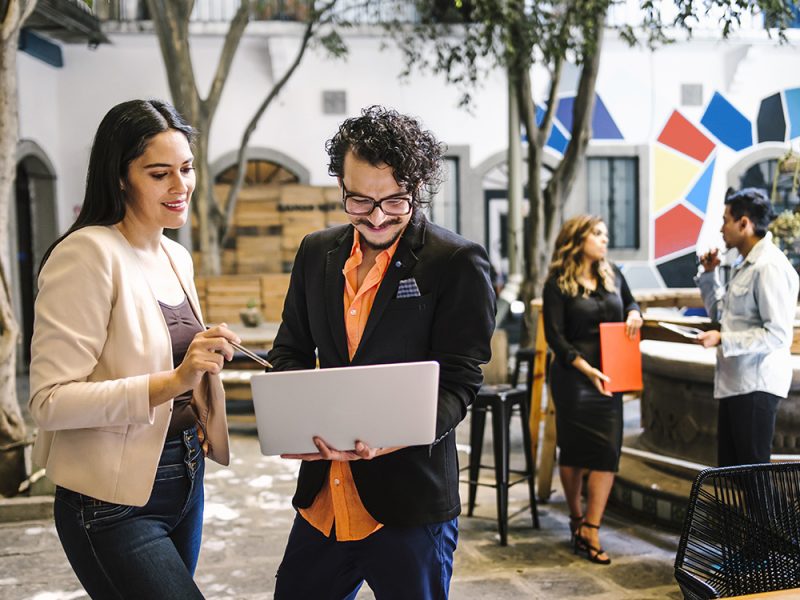 Two professionals reviewing work on a laptop in an open, colorful HR office setting