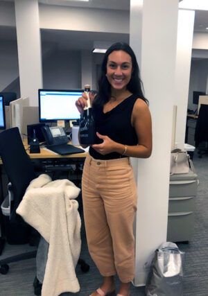 Smiling recruiter standing in an office holding a celebration bottle, recognized for her achievements in staffing and recruitment excellence