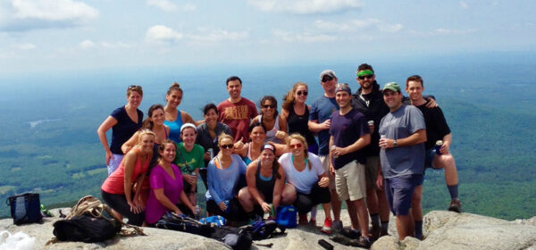 Group of recruiters enjoying a team-building hike on a mountaintop with scenic forest views in the background, showcasing a strong and collaborative staffing team