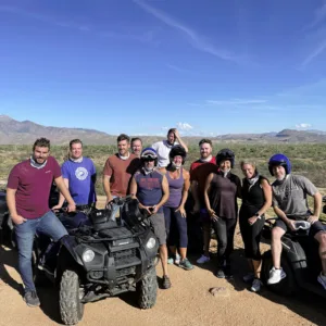 Group of recruiters posing with ATVs during a team-building desert adventure under a clear blue sky, highlighting camaraderie and outdoor fun in the staffing industry