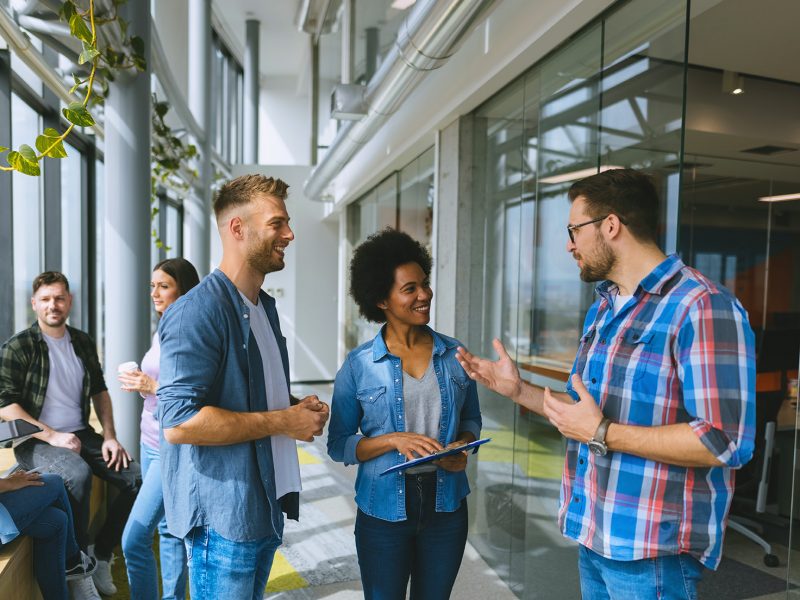A group of technology professionals engages in conversation and collaboration in a modern office setting. This image represents the approachable, people-first culture behind our staffing and consulting services—connecting companies with top tech talent and fostering environments where innovation and teamwork thrive.