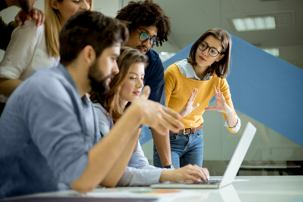 A group of professionals gathered around a laptop in a modern office, discussing workforce strategy and solutions.