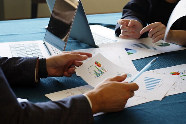 Two business professionals review workforce reports and charts at a table with open laptops.