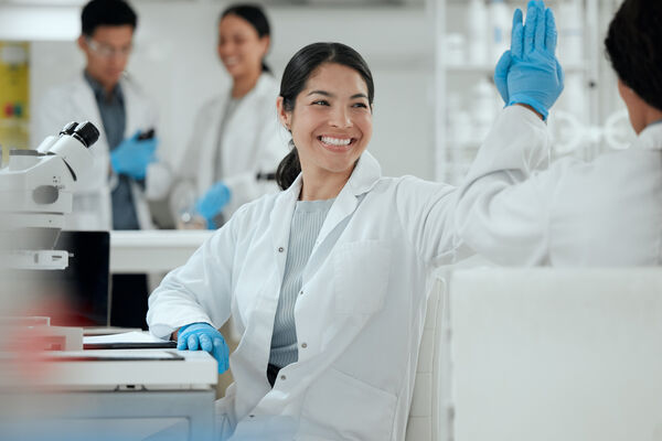 A team of happy scientists in lab coats celebrate with high fives in a bright, modern laboratory. This image captures collaboration, teamwork and scientific breakthroughs—perfect for showcasing a positive research environment.