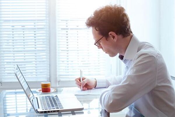 Professional man working at a laptop and taking notes, showcasing special skills in organization, focus and productivity in a bright office environment