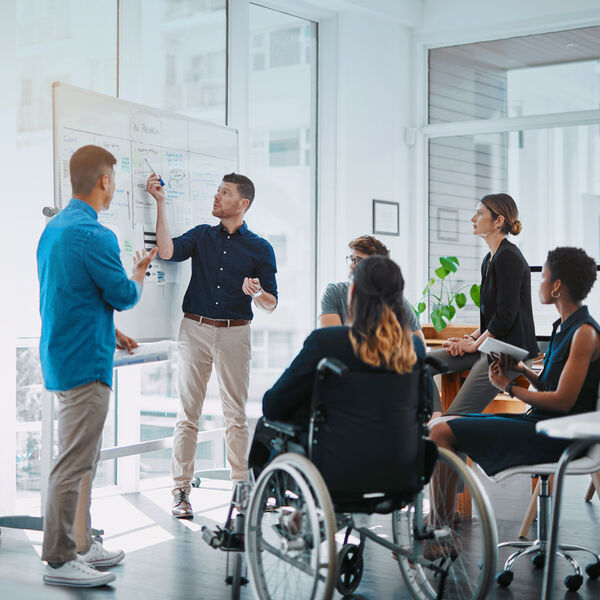 Team of professionals, including a person in a wheelchair, collaborating around a whiteboard during a financial planning session