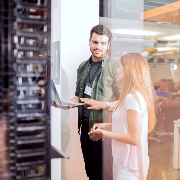 Two IT specialists collaborate in a data center environment, reviewing server infrastructure on a laptop. This image illustrates the technical expertise behind our consulting and staffing services—offering skilled infrastructure engineers, system administrators, and support professionals who keep enterprise systems secure, scalable, and optimized for performance.